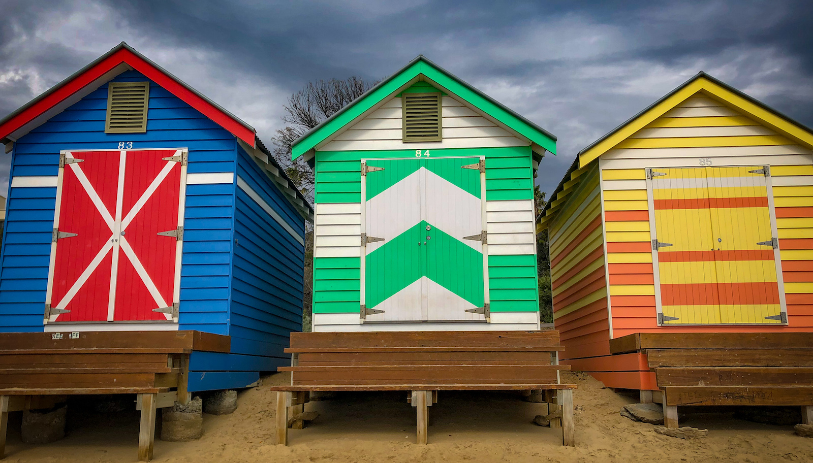 Three brightly colored huts rise from the sandy shore. What does one do in a bathing house?