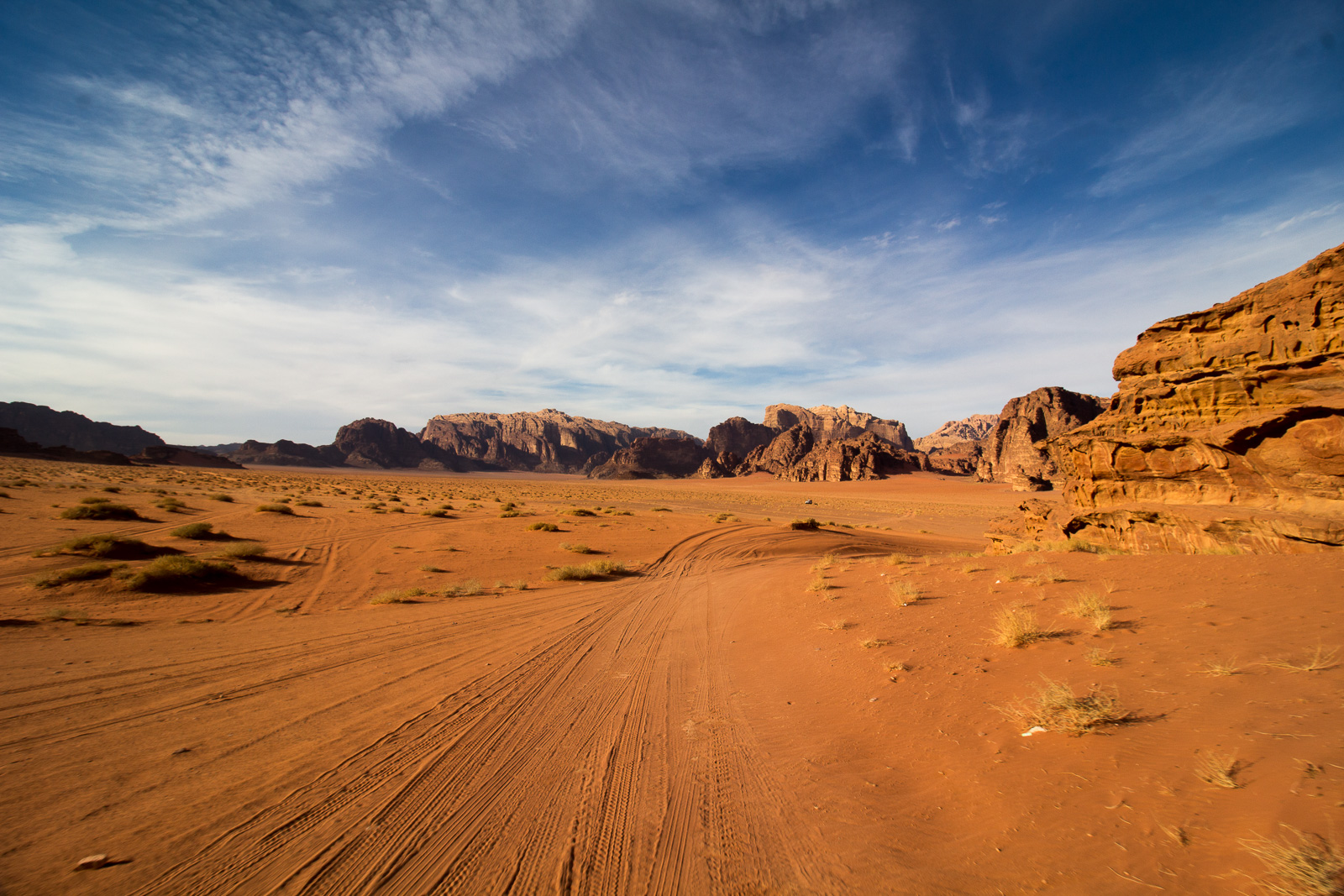 A wide view of the Mars-like terrain of Wadi Rum. So Mars-like that it's where they shot The Martian. Tire tracks follow behind.